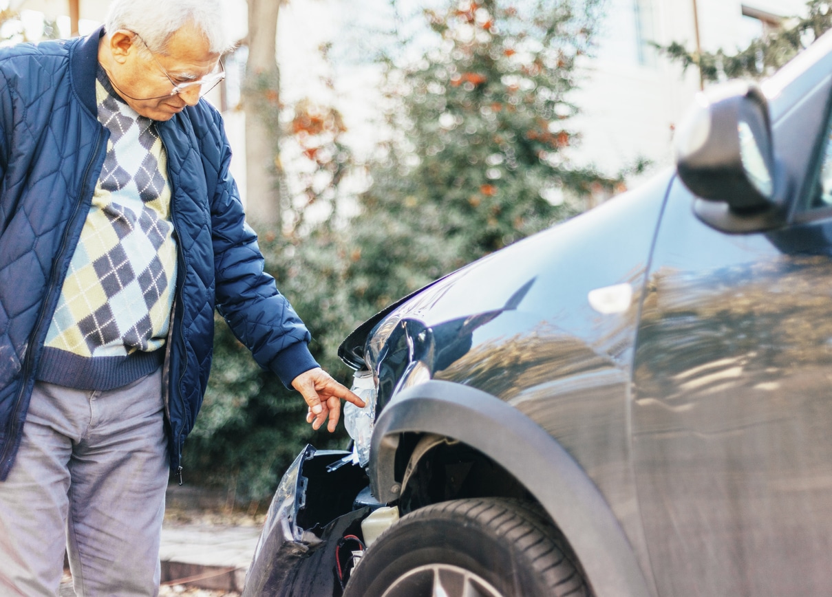 older man checking out damage to car after accident