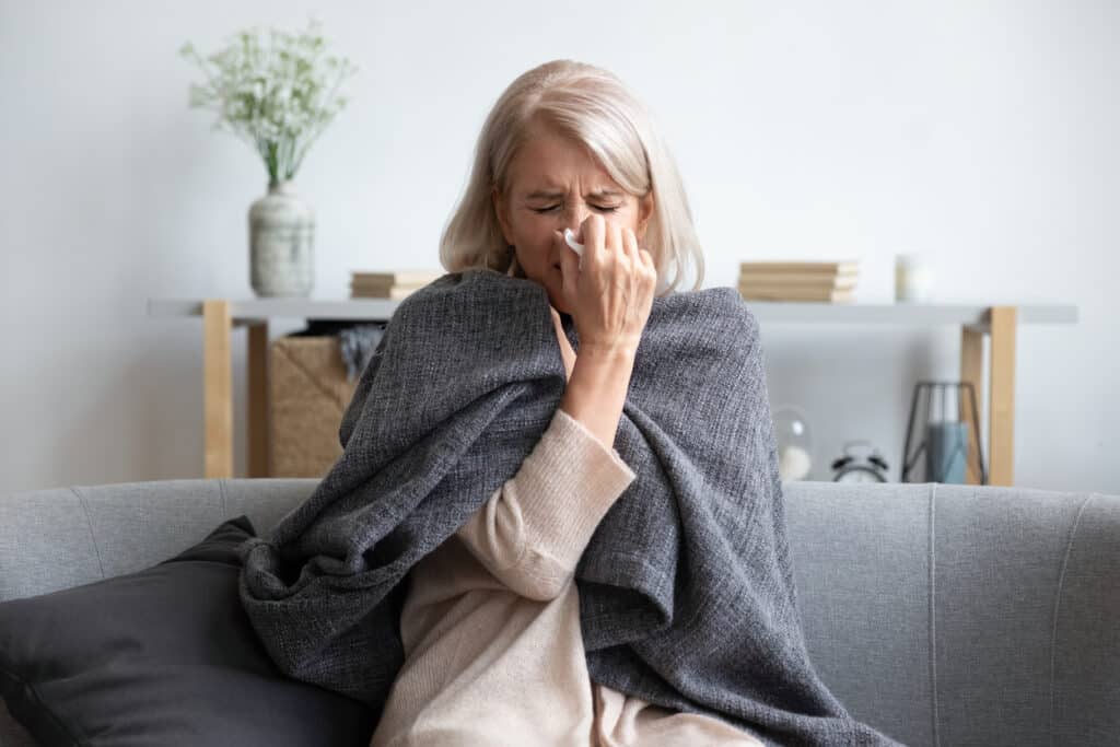 Senior woman sick with flu sneezing holding napkin blow out runny nose