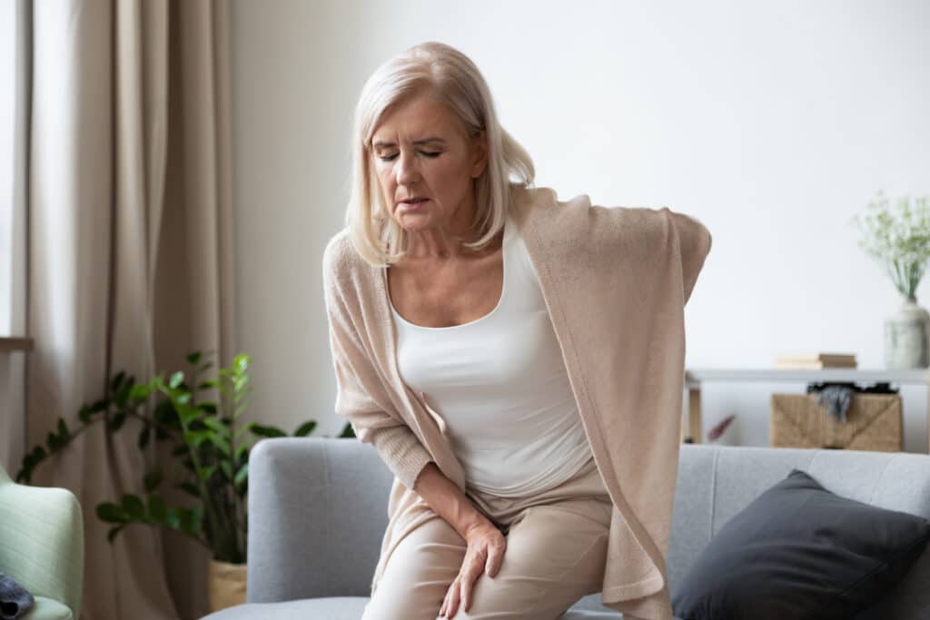 Elderly 60s woman got up from couch felt severe painful feelings in lumbar, massaging low back to reduce ache, suffer from backache discomfort, diseases of older people, sciatic nerve injury concept