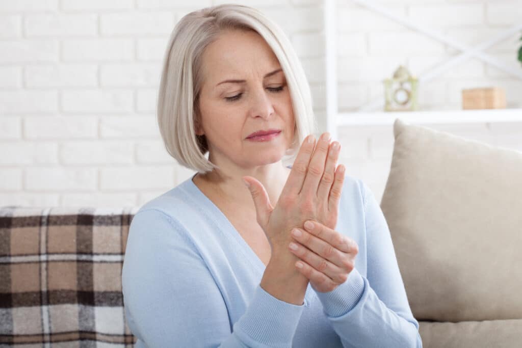 Middle aged woman suffering from Osteoporosis pain in hands, closeup. Woman massaging her arthritic hand and wrist