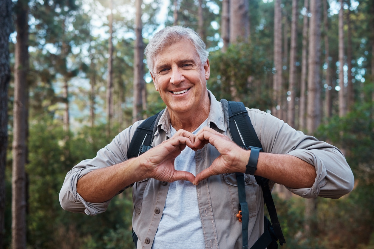 Shot of a mature man forming a heart shape with his hands while out hiking