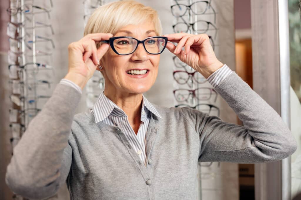Smiling senior woman trying prescription glasses in optician store. Healthcare and medicine
