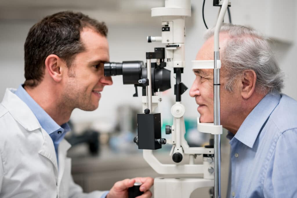 Portrait of a senior patient getting an eye exam at the optician on the phoropter - healthcare and medicine concepts