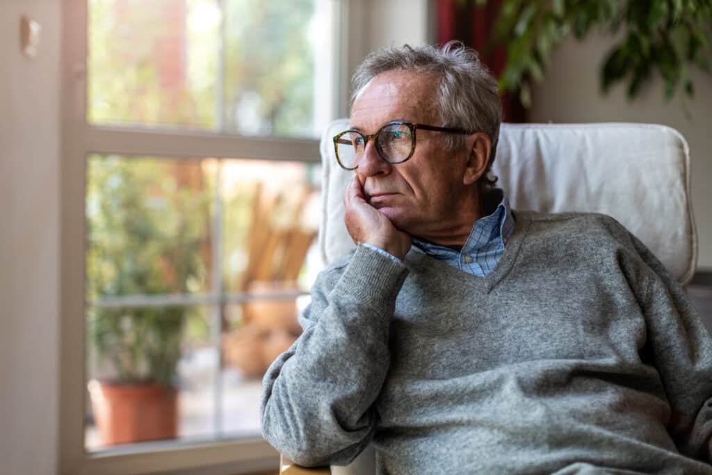 senior man suffering from depression looking out of a window at home.