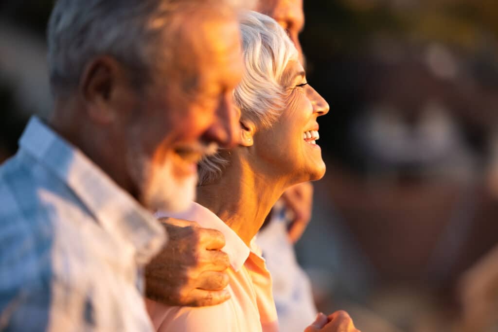 Happy mature woman walking embraced with her friends at senior living community.