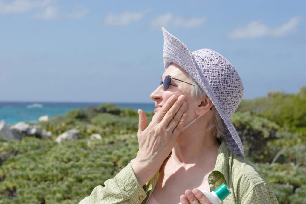 senior women outside hiking along coast putting on sun block to protect against skin cancer.