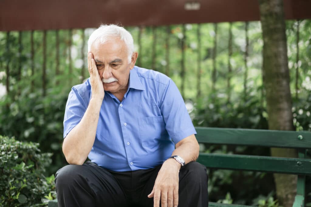 Portrait of a senior Caucasian man feeling depressed, sitting on a park bench, thinking and contemplating something in his mind