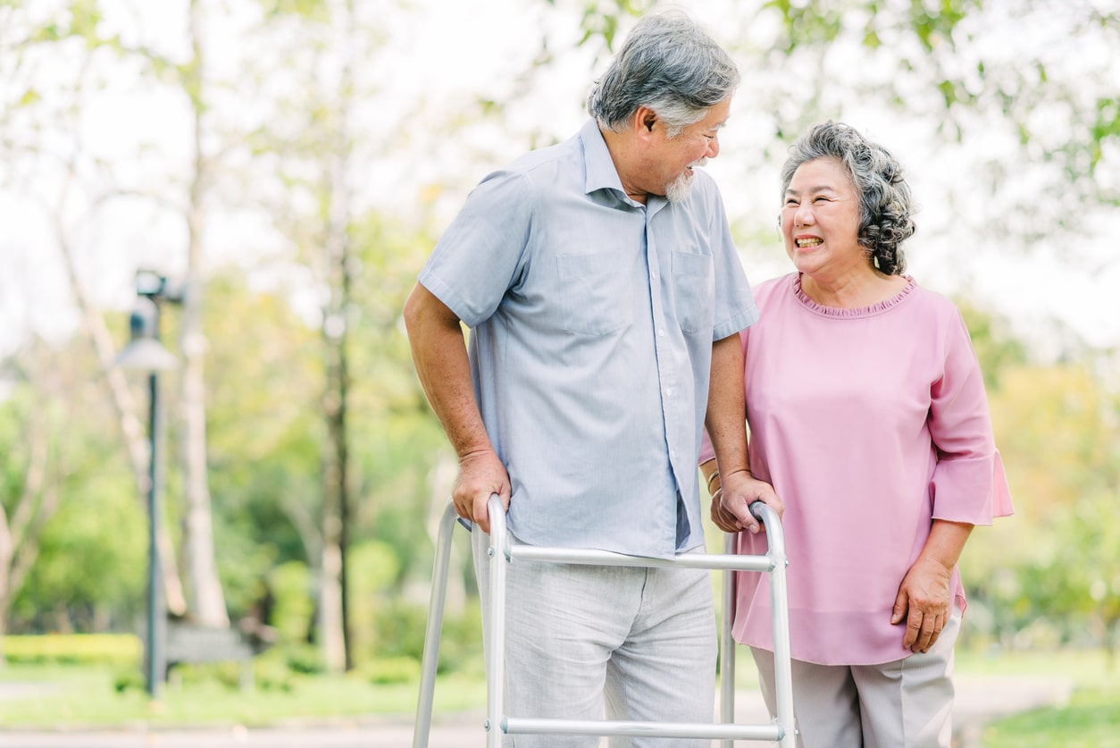 senior Asian couple laughing while walking with walker to prevent fall risk
