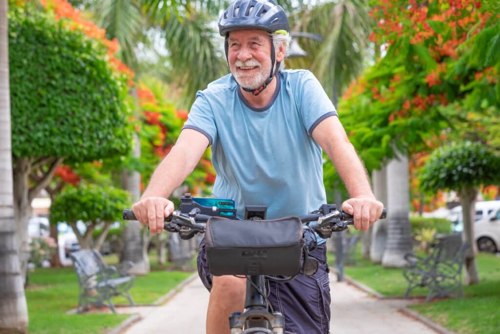 Happy active senior man cycling in the public park with electric bicycle enjoying freedom. Concept of healthy lifestyle and lowering high blood pressure