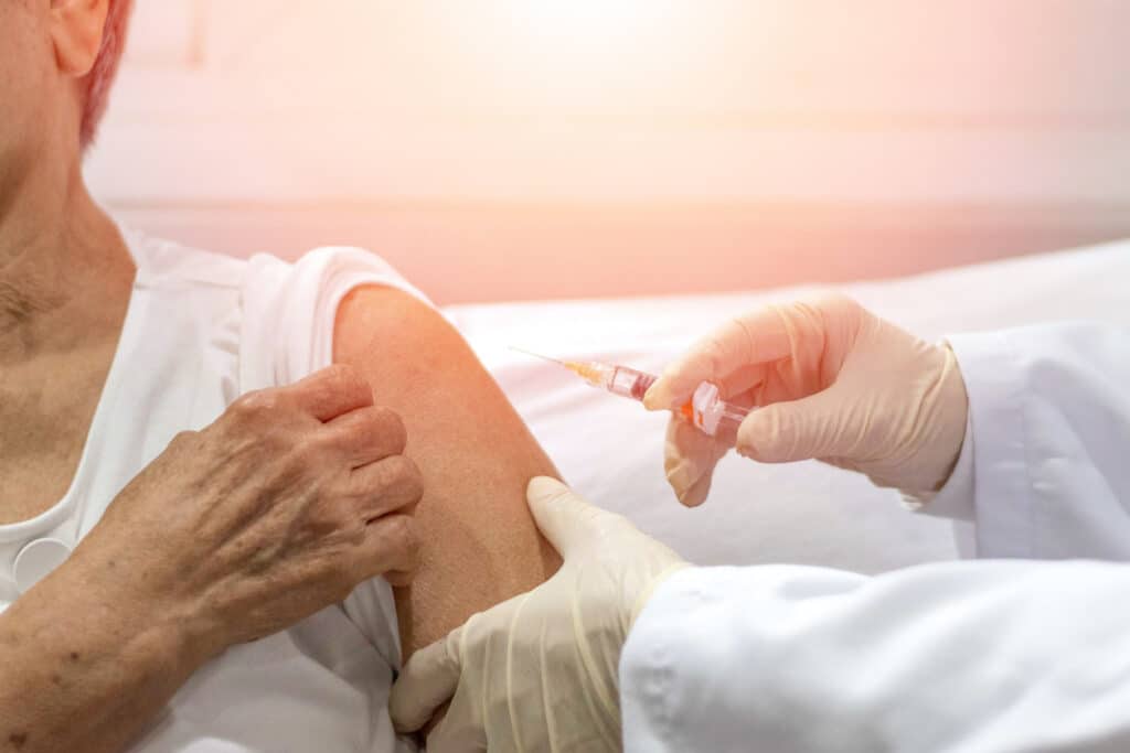 Senior vaccination concept. Elderly getting immune vaccine at arm for flu shot, pneumonia, and shingles(MMR) in hospital by nurse. Doctor giving an injection to older people patient in clinic.