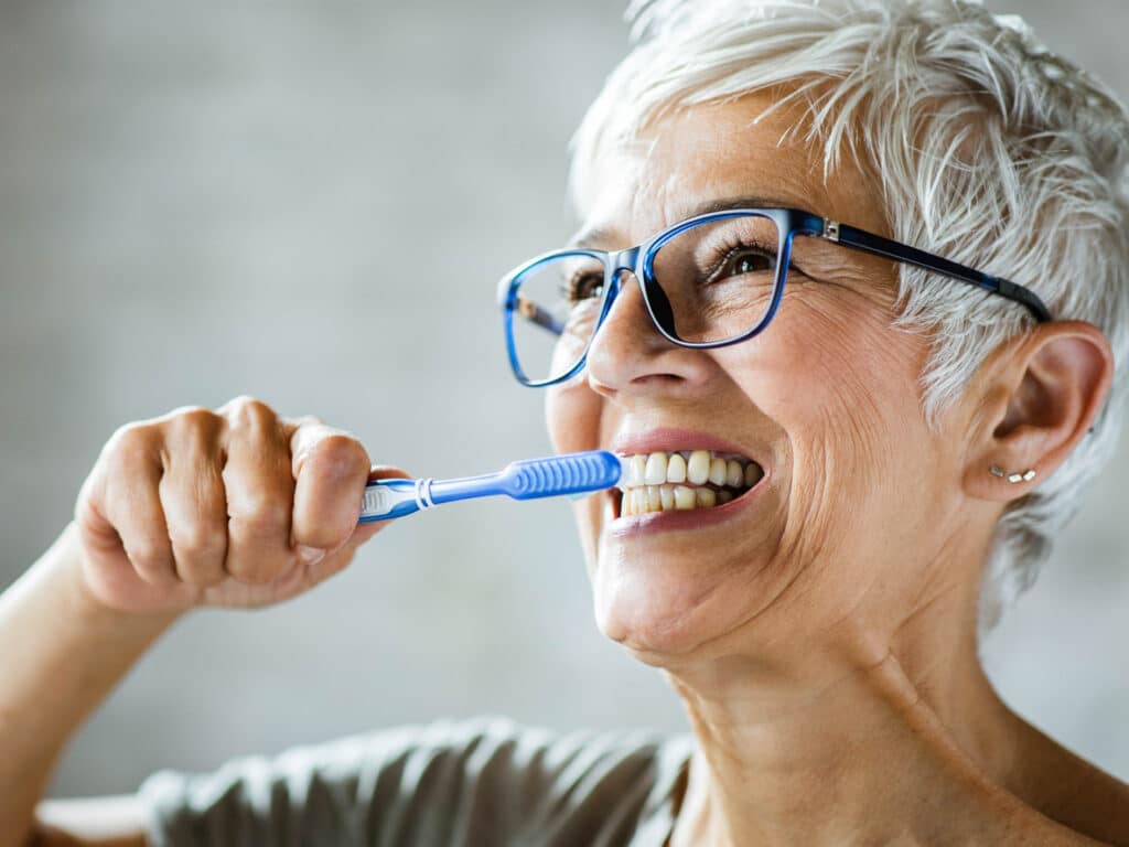 Happy mature woman brushing her teeth.