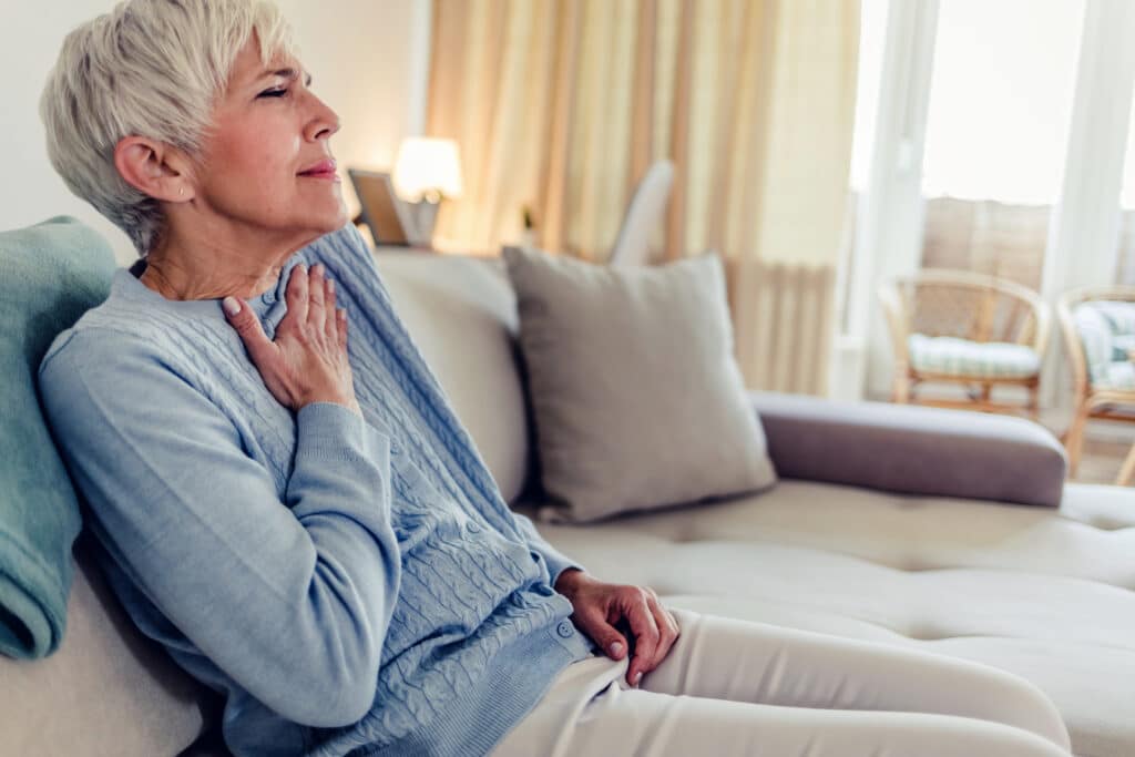 senior women with chest pain from pneumonia. Women sitting out couch in living room holding chest in pain.