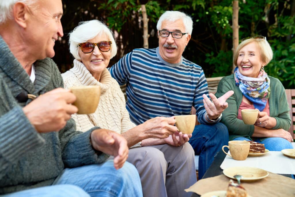 Cheerful group of senior friends enjoying each others company while having tea party at lovely patio, they wearing knitted sweaters