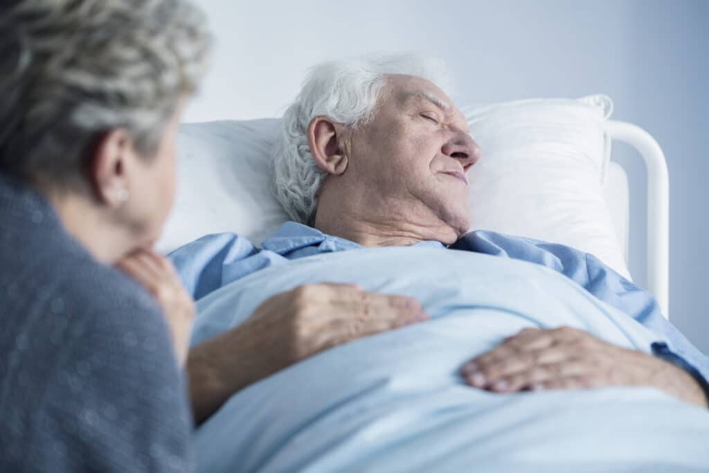 Elderly patient in hospital bed with pneumonia with wife by his side